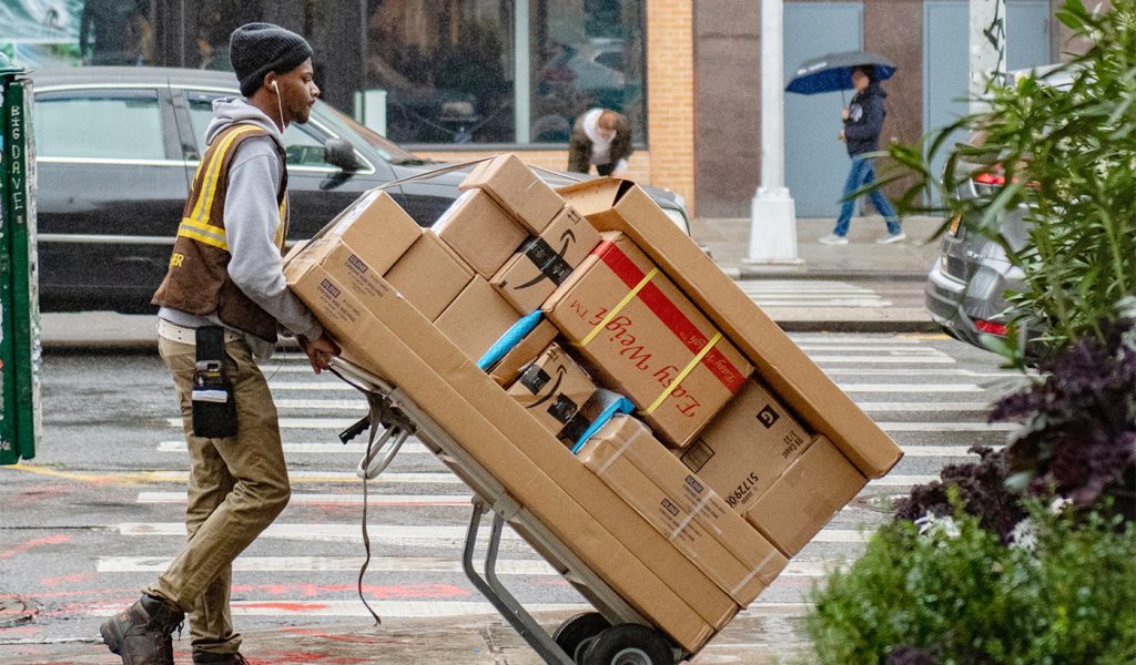 Delivery driver crossing the street with a sack truck full of different parcels